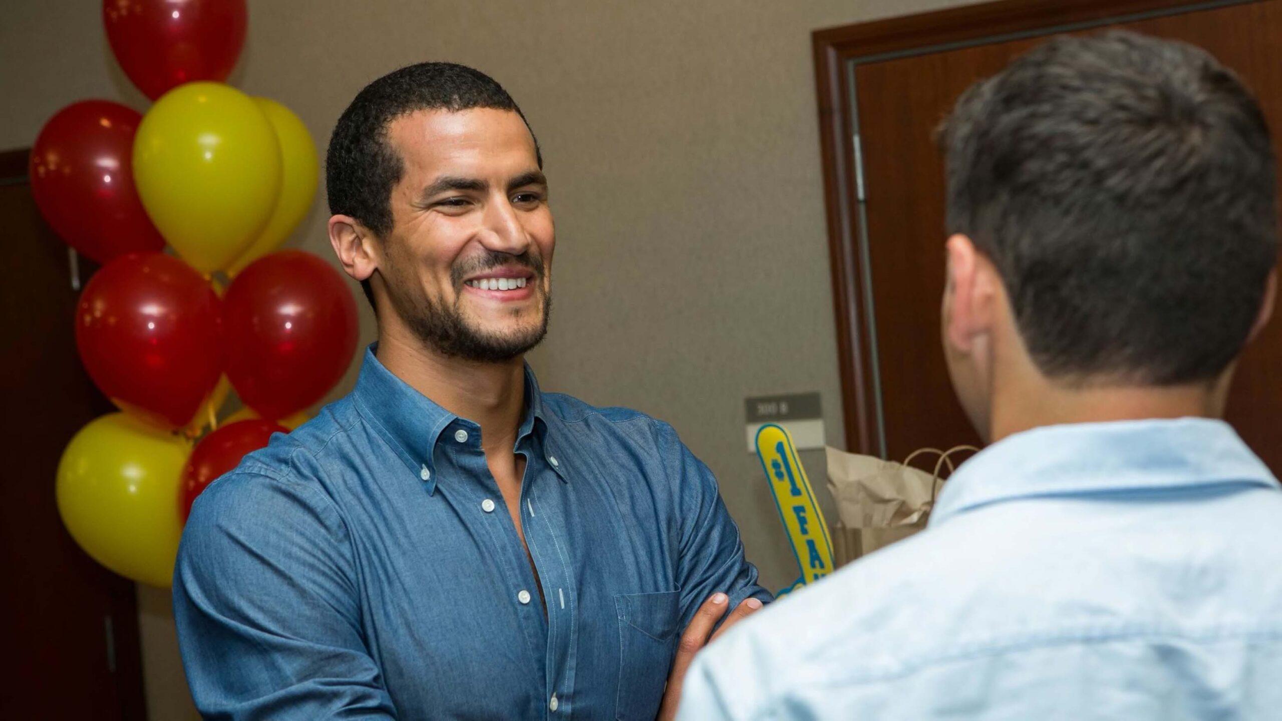 man smiles in front of red and yellow balloons